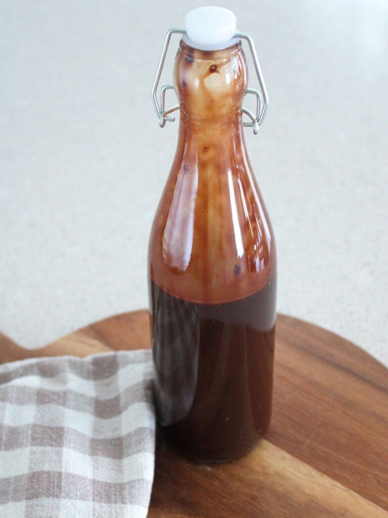 Syrup cooled and stored in a glass container on a cutting board with a plaid napkin