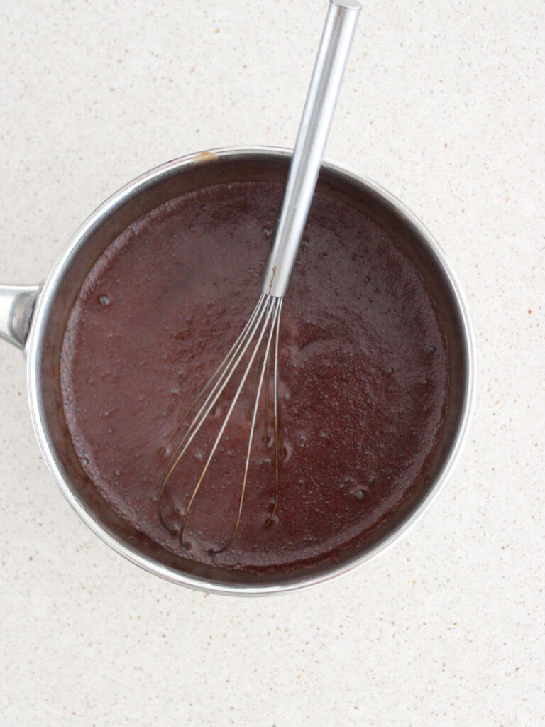 Adding Vanilla to the syrup with a whisk in a stainless steel saucepan