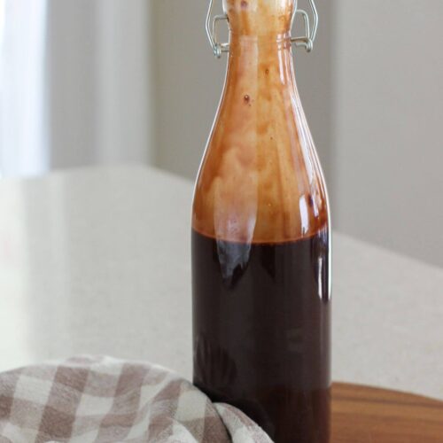 Homemade Chocolate Syrup in a bottle on a cutting board with a plaid napkin next to it