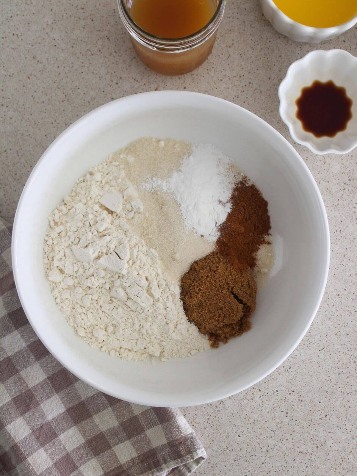dry ingredients mixed in white bowl with small bowls of wet ingredients around and a plaid napkin
