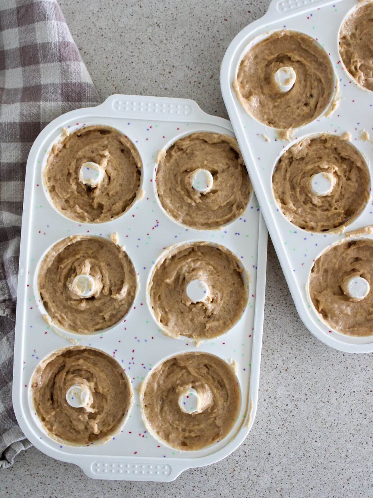 Donuts in a silicon donut mold ready to bake with a plaid towel next to it