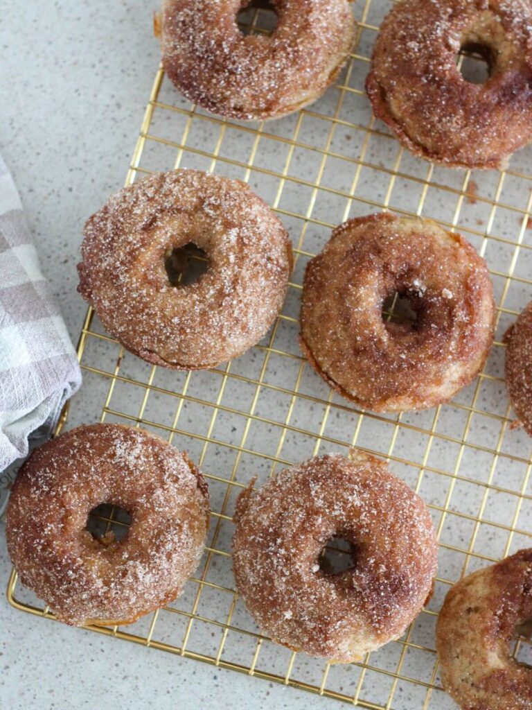 finished donuts on a golden cooling rack with a plaid napkin next to it 