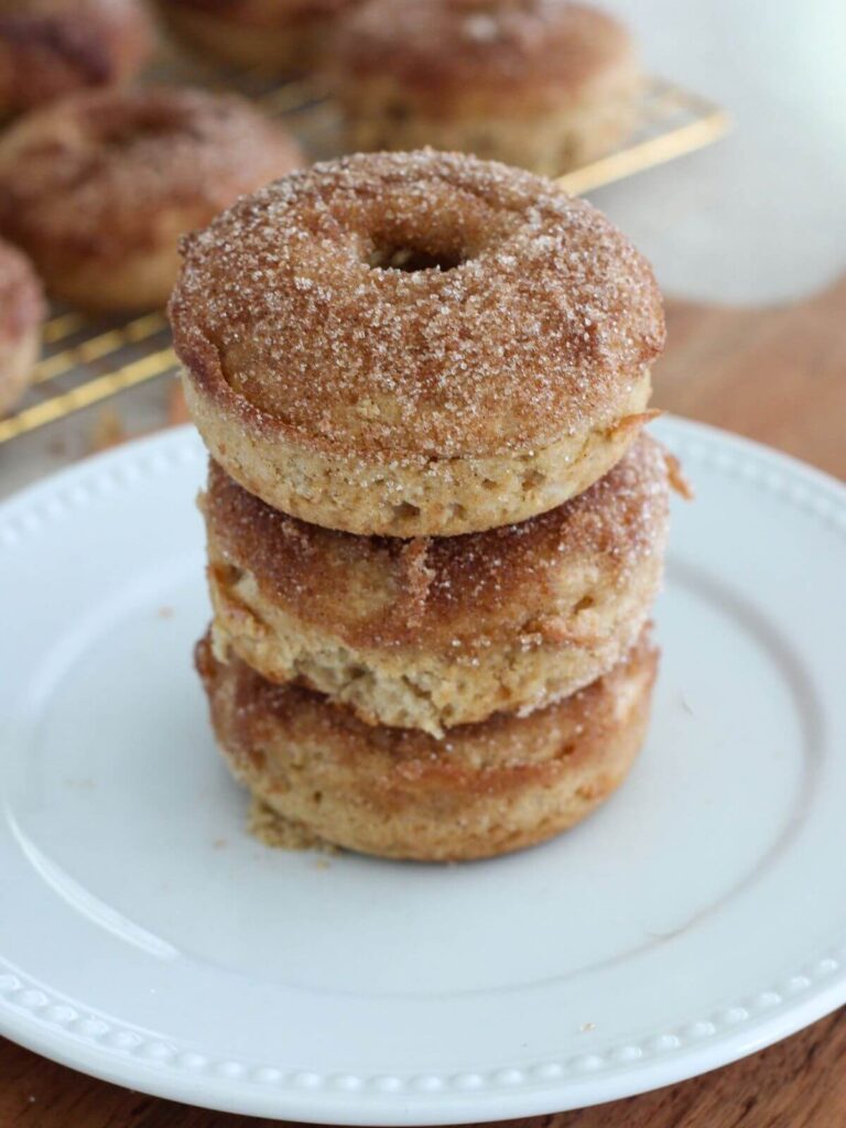 Baked Apple Cider Donuts Stacked 3 high on a white plate with rest of the donuts in the background