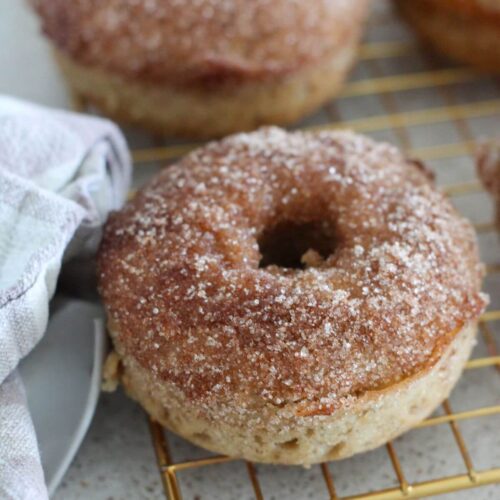 Baked apple cider donut up close on a golden cooling rack with a plaid napkin