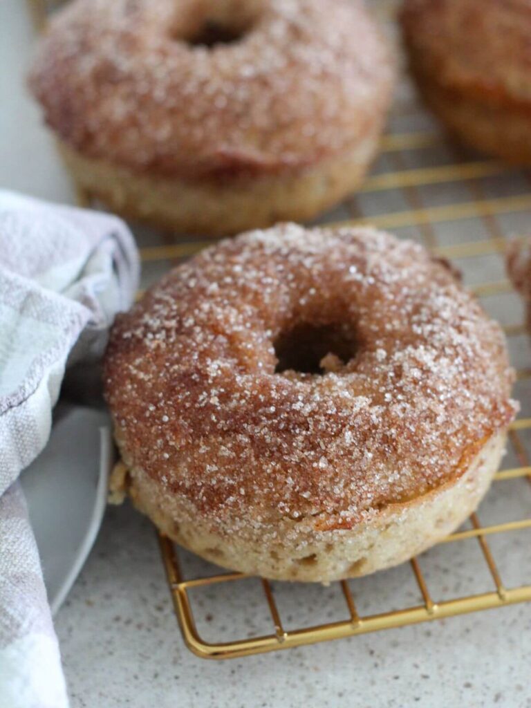 Baked apple cider donut up close on a golden cooling rack with a plaid napkin