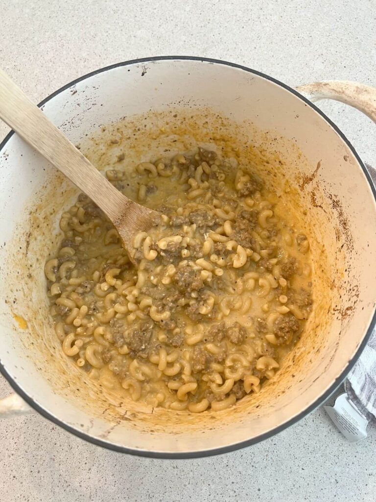 cheesy hamburger helper in a white dutch oven with a wooden spoon 