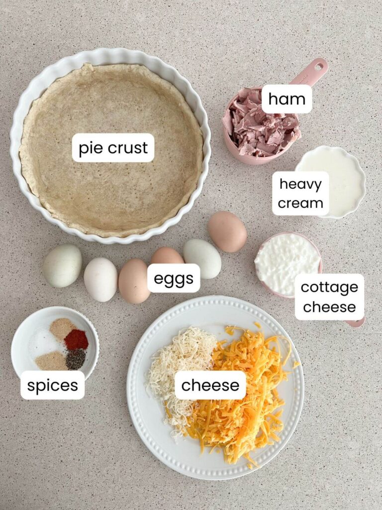 An ingredient flat-lay of what is needed for he recipe. A pie crust, ham, heavy cream, cottage cheese, cheese, eggs, spices