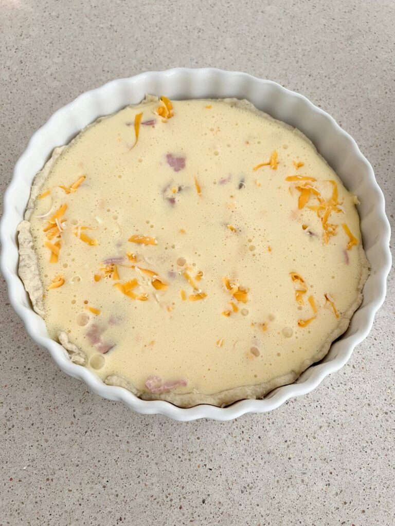Egg mixture poured over ham and cheese mixture and ready to bake in pie crust
