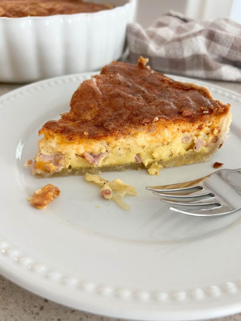 quiche on a white plate ready to eat with a silver fork next to it.