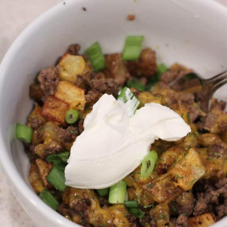 potatoes, meat and cheese in a white bowl ready to eat topped with sour Cream and green onions.