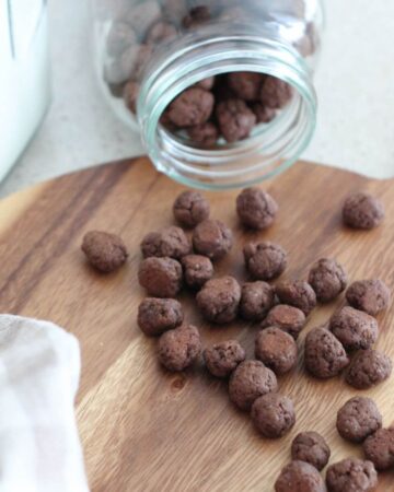 healthy Cocoa Puffs on a brown cutting board spread out from a glass mason jar with a plaid towel next to it.