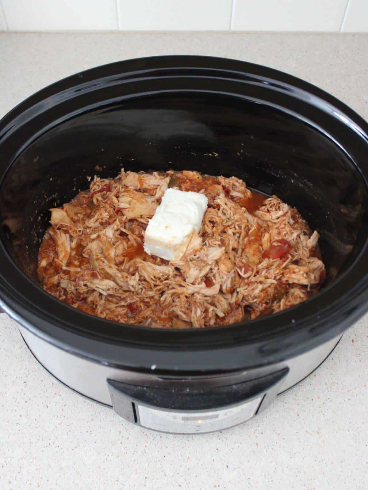 Adding cream cheese to the shredded chicken in the crockpot.