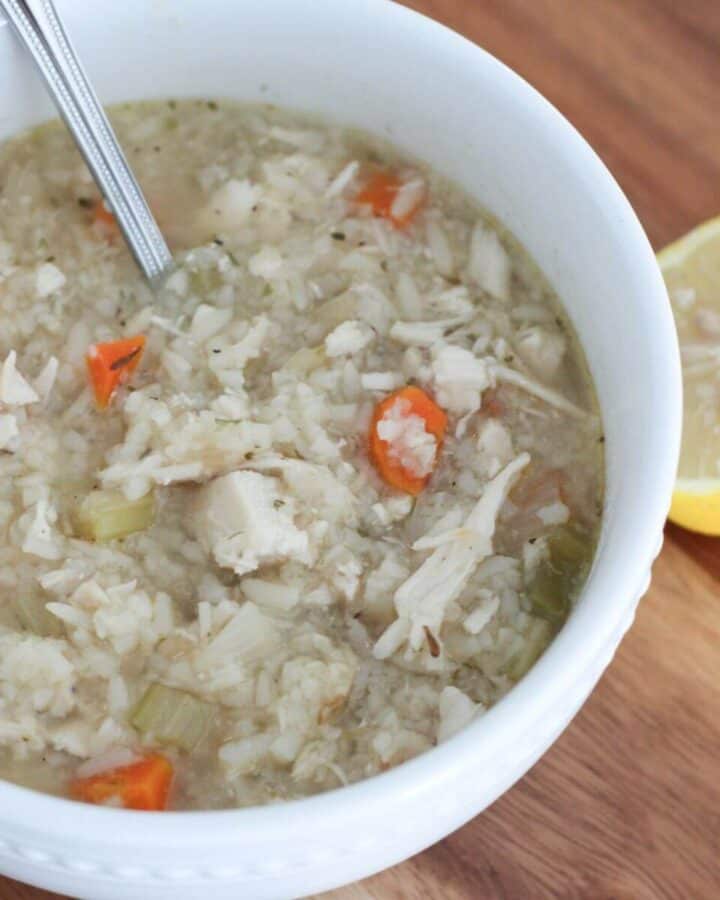 Crockpot Chicken and Rice Soup in a white bowl with a silver spoon on a cutting board with a lemon next to it ready to eat.