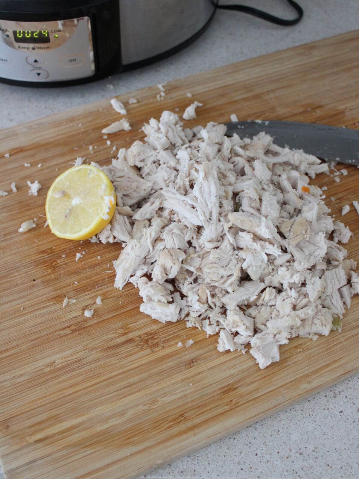 Chicken shredded on a cutting board with a lemon next to it with the crockpot in the background.