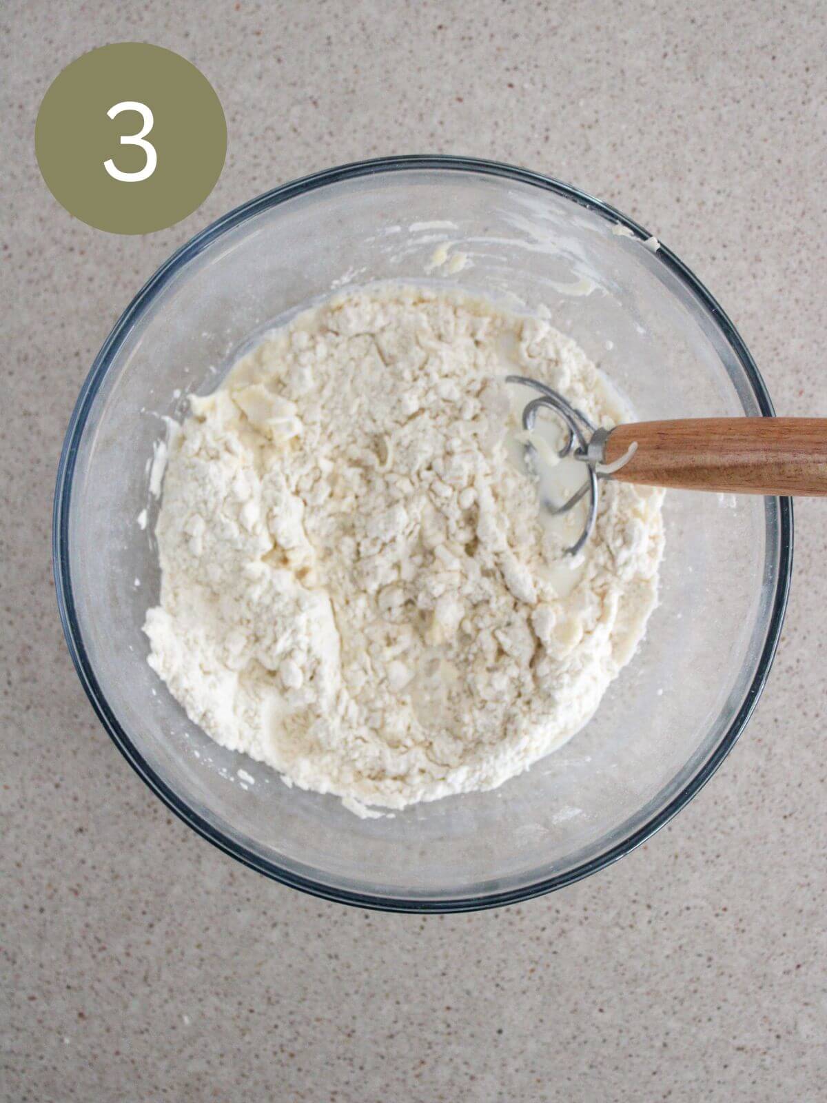 milk added to the mixture in a clear glass bowl with a dough whisk