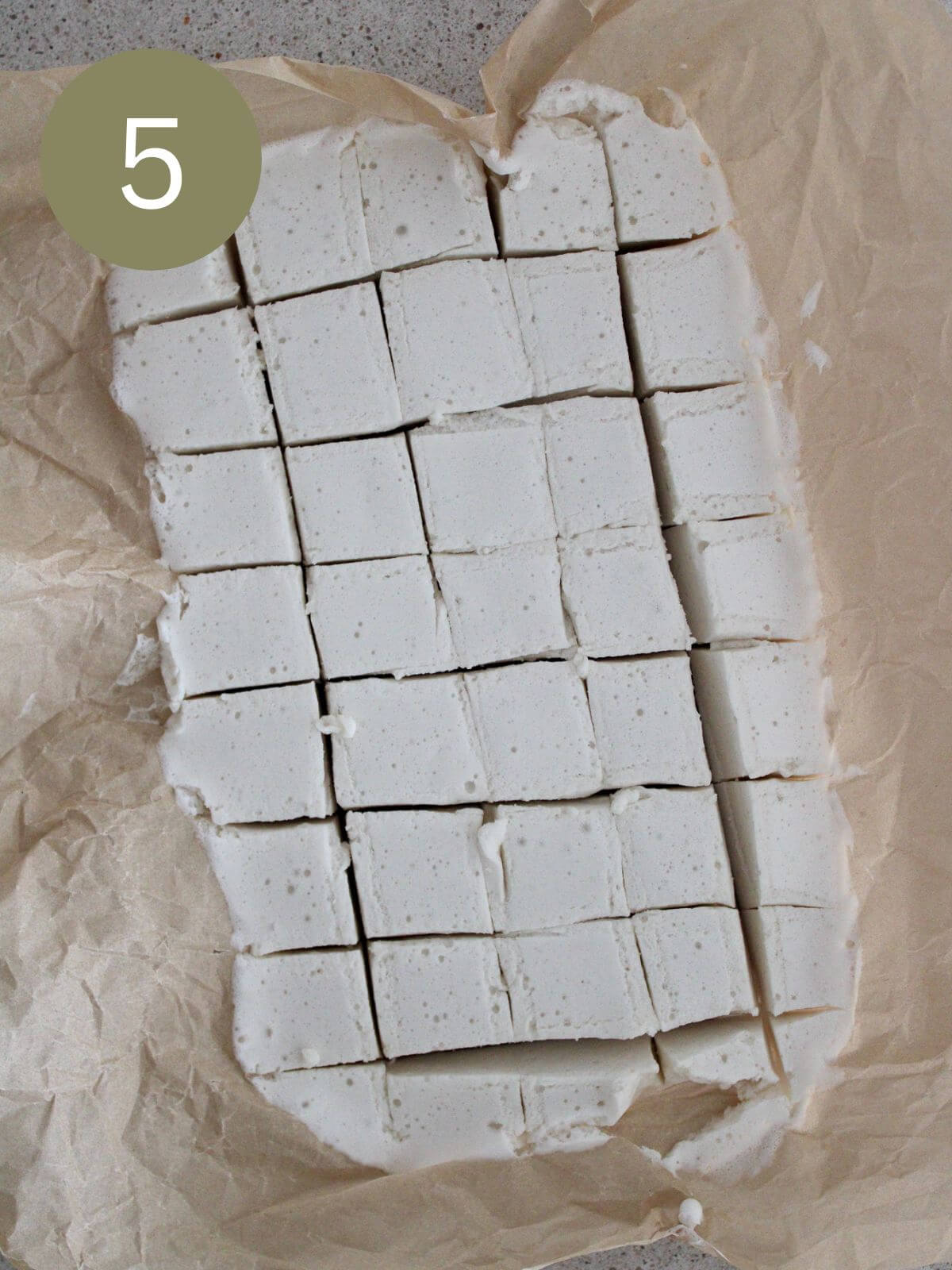 Marshmallows cut into squares with powdered sugar on top in a glass pan with parchment paper