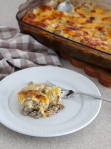 biscuits and gravy casserole on a white plate with a silver spoon with the 9x12 baking pan in the background and a plaid napkin