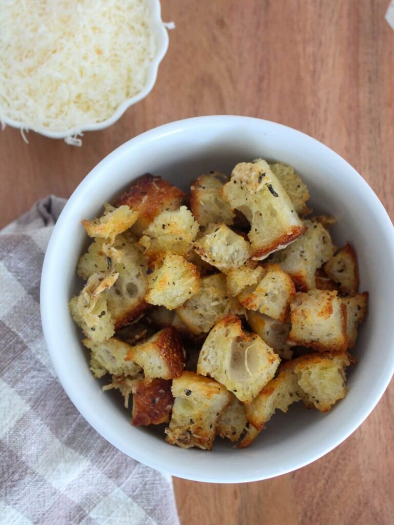 Parmesan croutons in a white bowl ready to eat with a plaid napkin and small white bowl of parmesan
