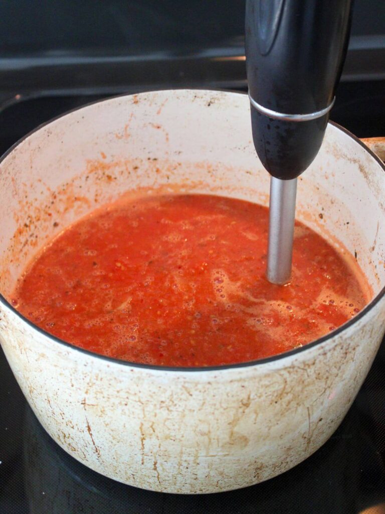 Immersion blender blending the soup in white dutch oven 