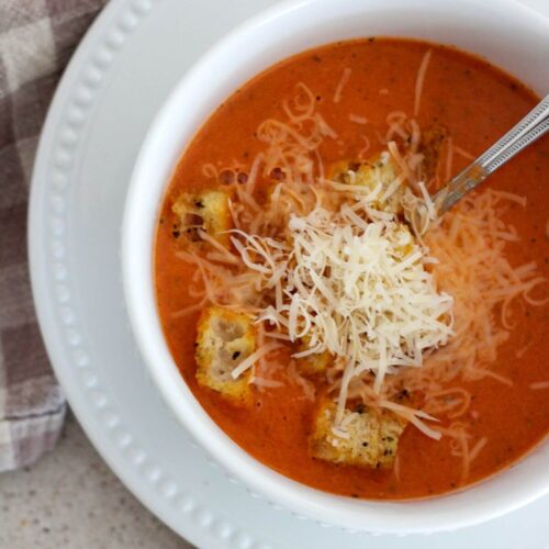 Best Creamy Tomato Soup up close in a white bowl with a white plate underneath with a plaid napkin