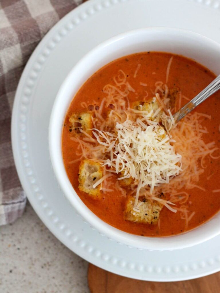 Best Creamy Tomato Soup up close in a white bowl with a white plate underneath with a plaid napkin 