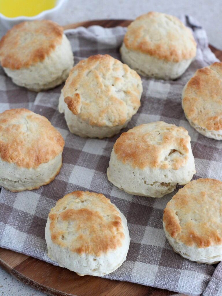 Up close picture of the biscuits on a plaid napkin on a cutting board with a small white dish of melted butter