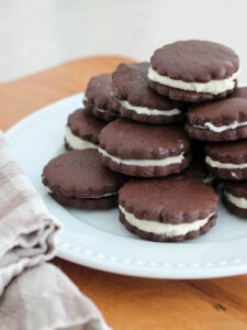 Homemade Oreo Cookies stacked on a white plate on a cutting board with a plaid napkin