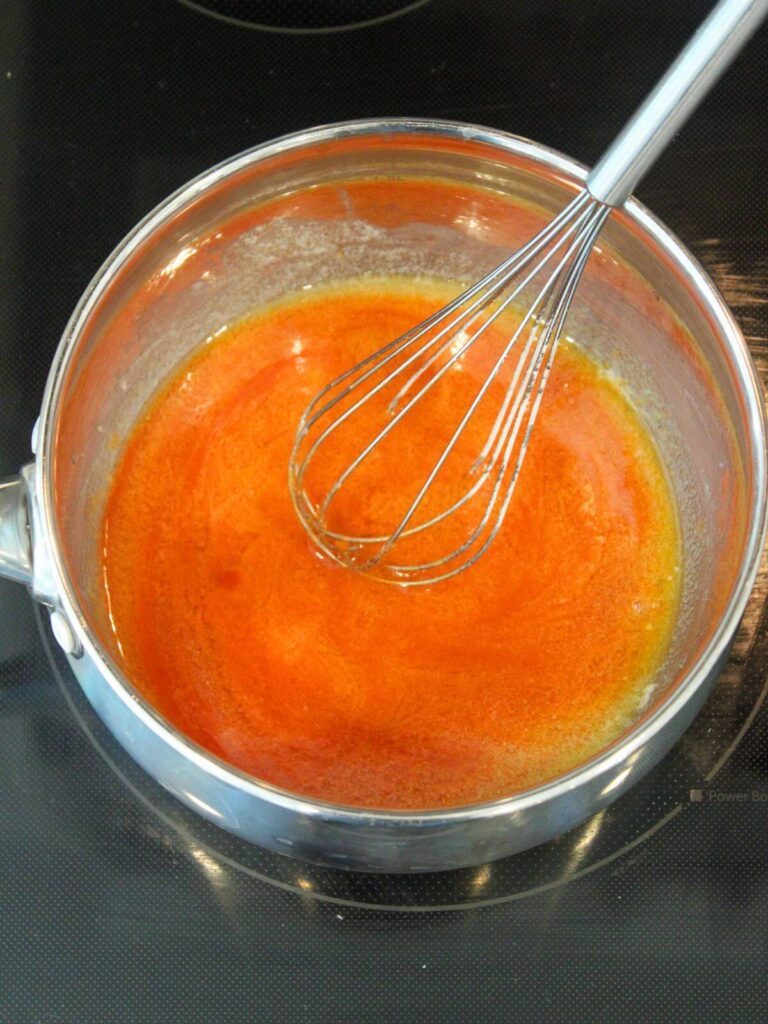 Whisking the hot sauce into the butter and flour in a stainless steel plan with a stainless steel whisk