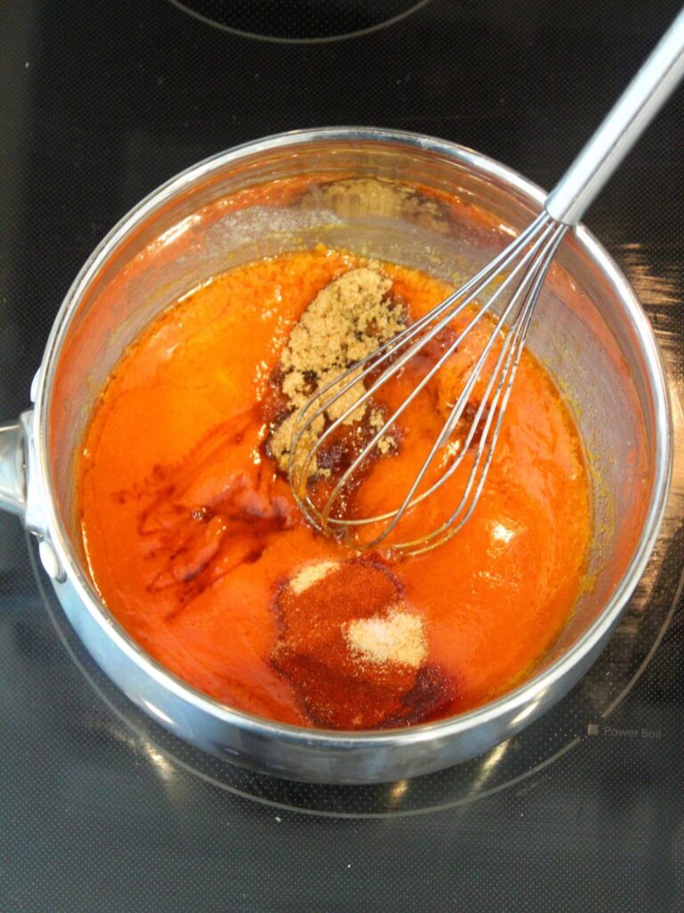Adding brown sugar, honey, paprika and garlic powder to the hot sauce mixture in a stainless steel pain with a metal whisk
