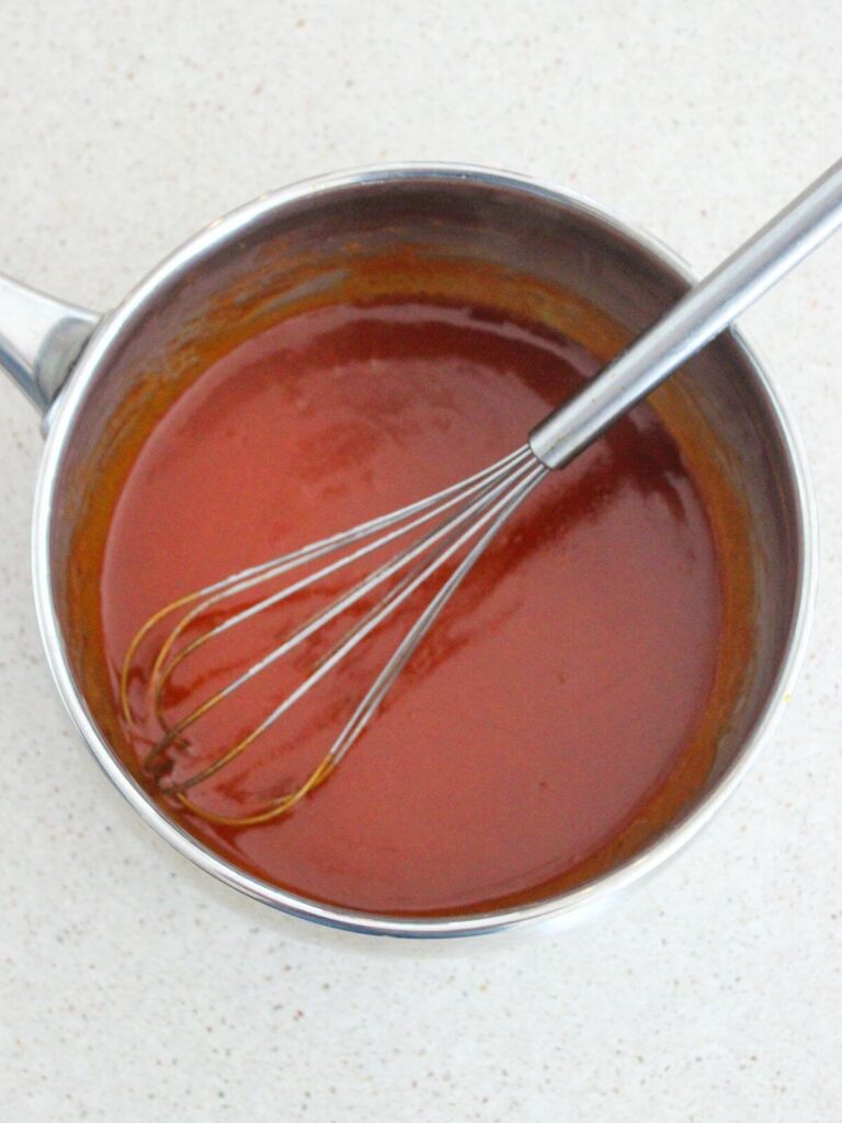 Sweet Buffalo hot sauce cooling in a stainless steel pan with a metal whisk