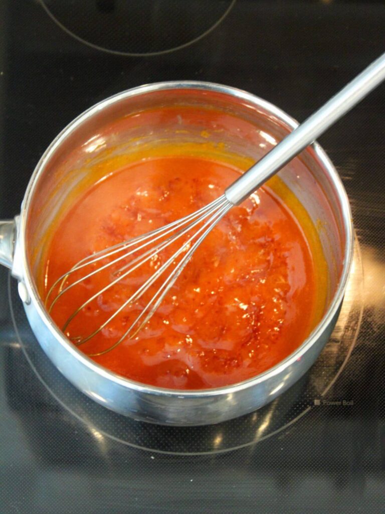 Hot sauce mixture simmering in a stainless steel pan with a metal whisk