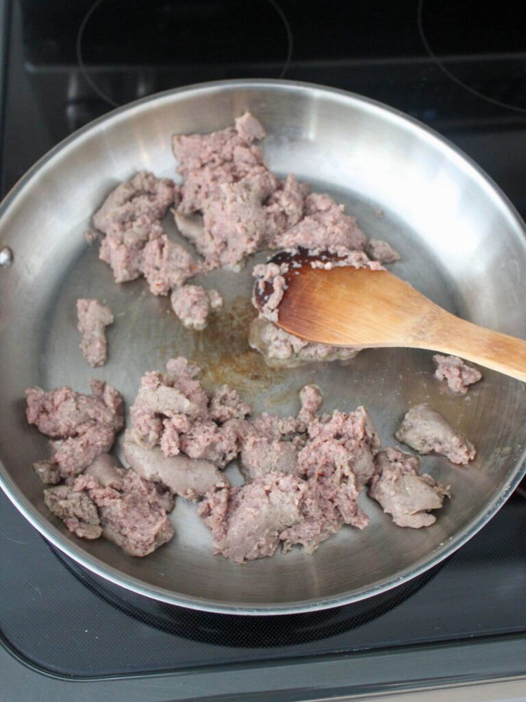 sausage browning in a stainless steel pan with a wooden spoon