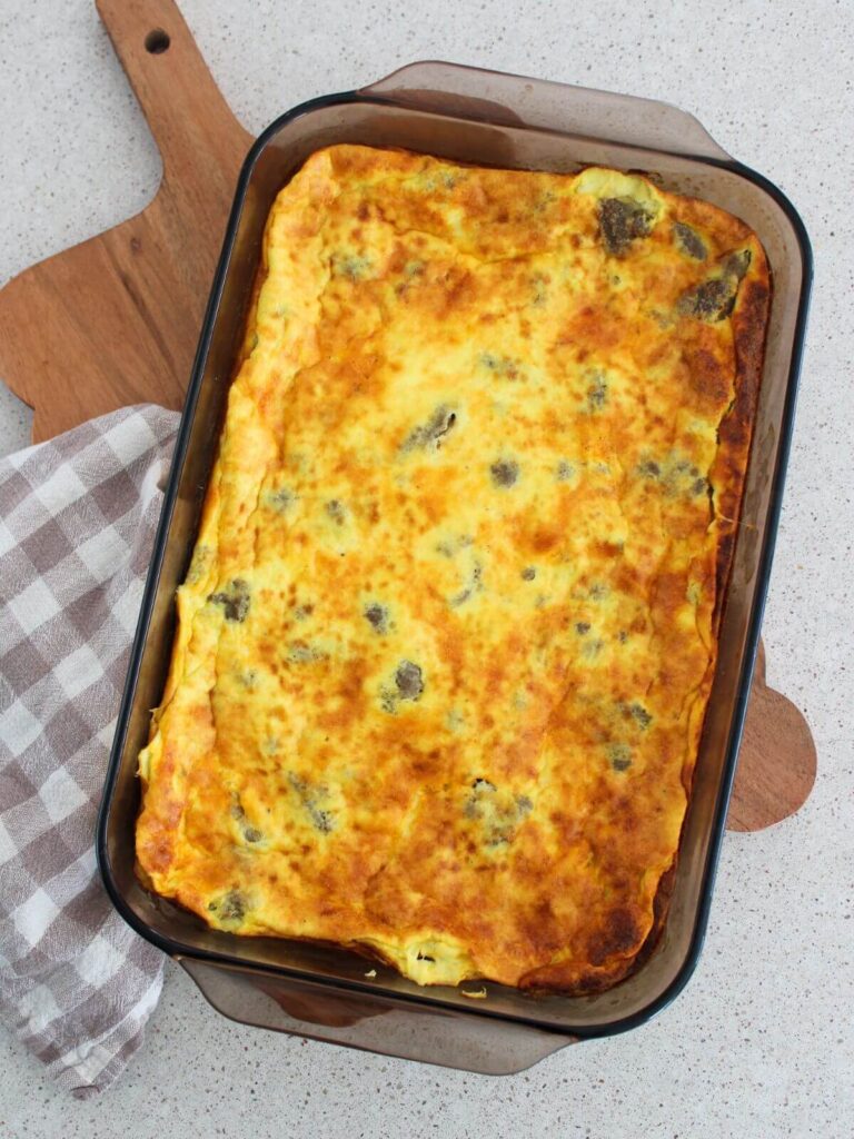 Egg and sausage bake in a brown glass pan on a cutting board with a plaid napkin