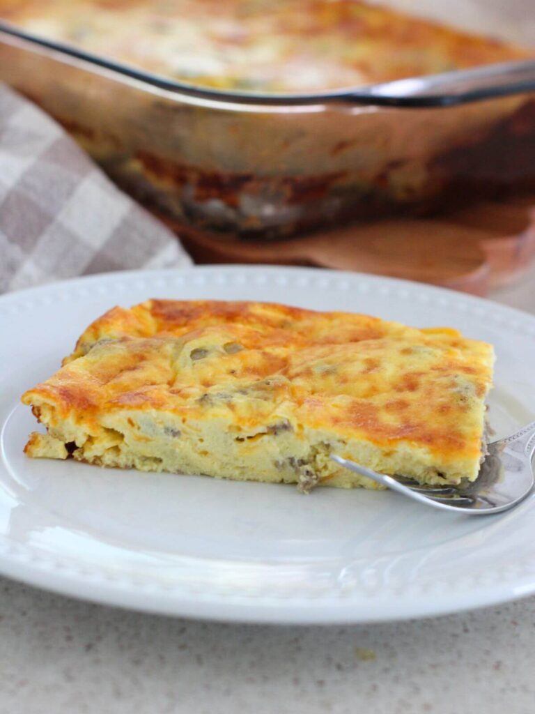 a close up side view of the egg and sausage bake on a white plate with the rest behind it with a plaid napkin