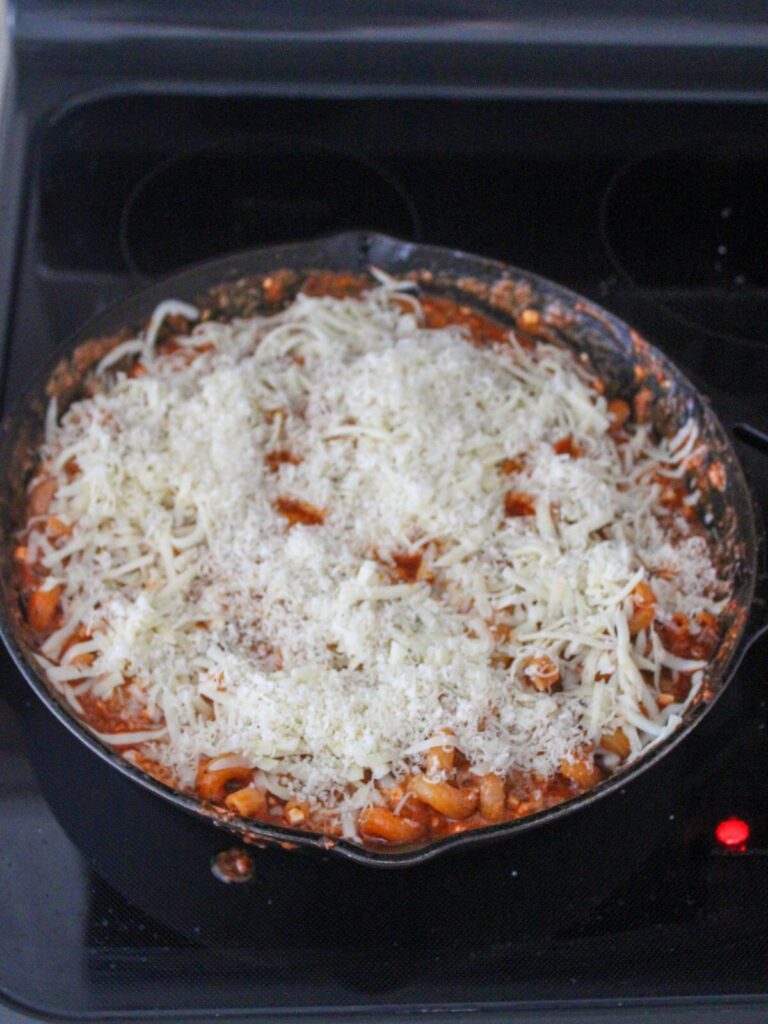 adding the parmesan and mozzarella cheese to the top of the pasta bake in the cast iron skillet 