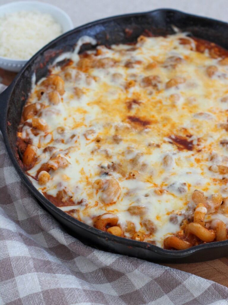 the pasta bake resting on a cutting board in the cast iron skillet with a plaid towel next to it