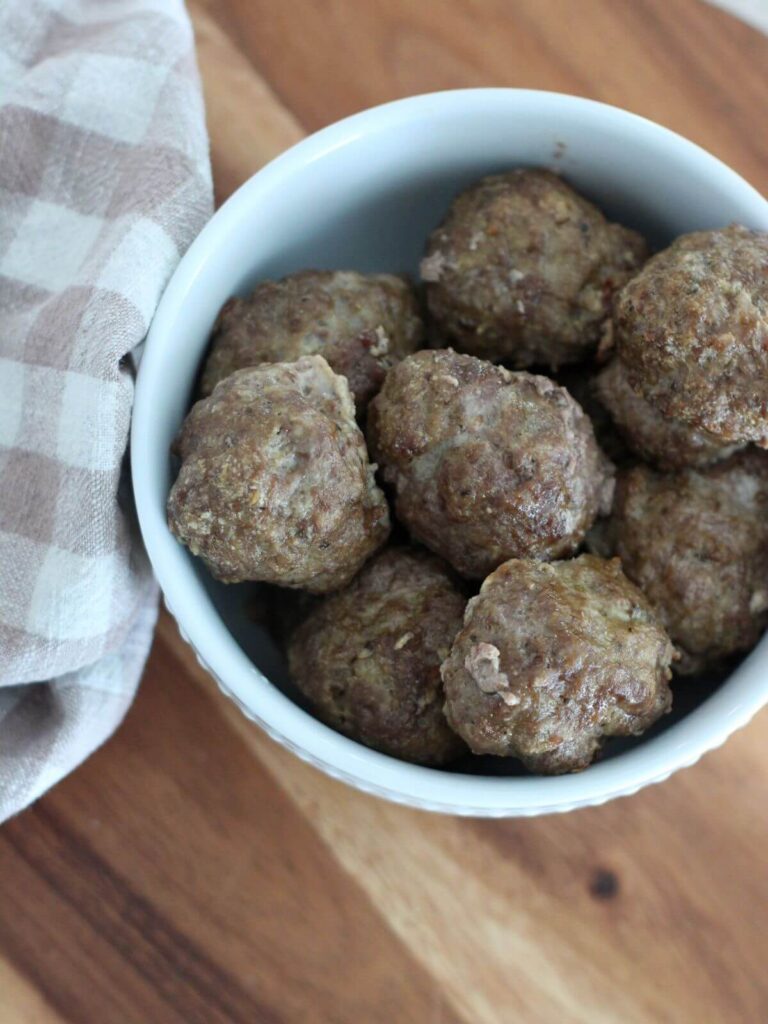 Meatballs in a white bowl on a cutting board with a plaid napkin