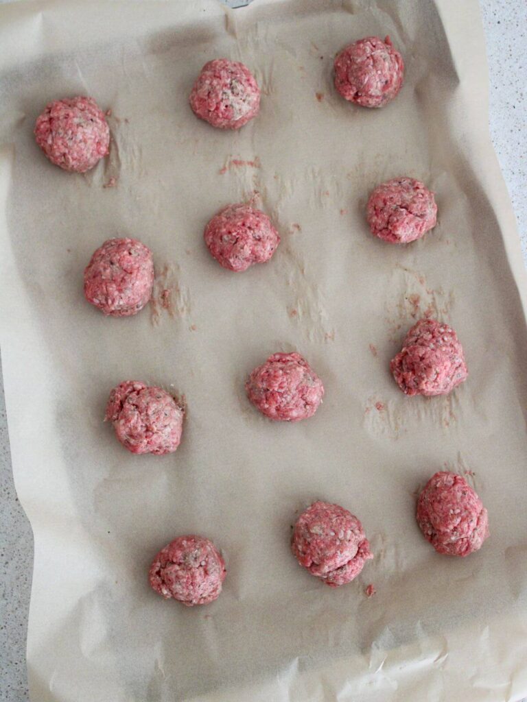 meatballs rolled into balls on parchment lined baking sheet