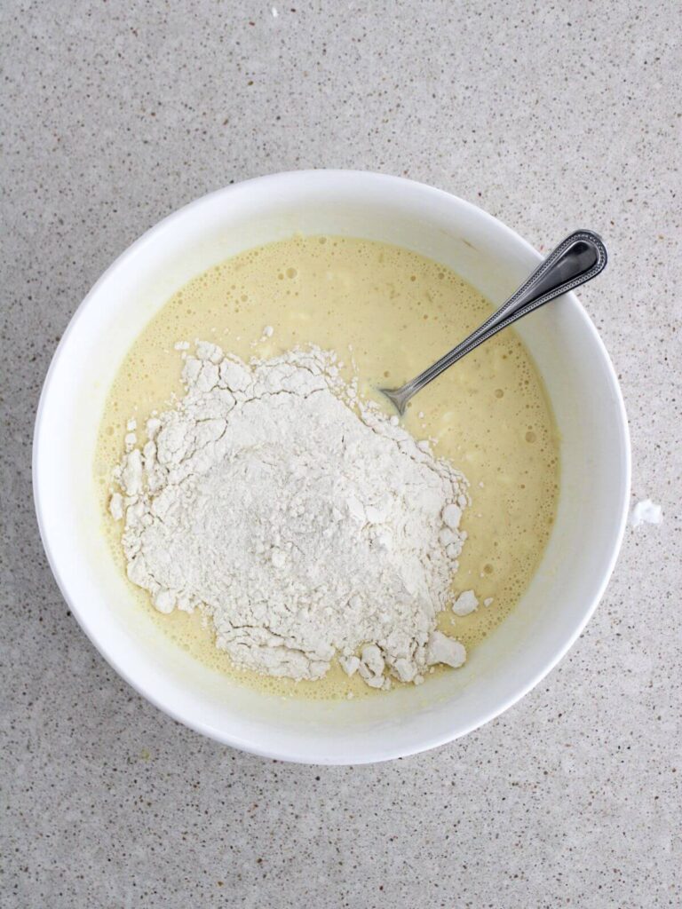 Combining the wet ingredient with the dry ingredients in a white bowl with a silver spoon
