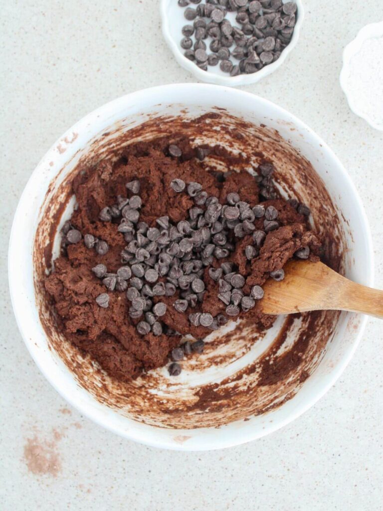 folding in the chocolate chips into the mixture in a white bowl with a wooden spoon