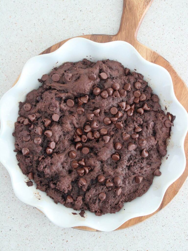 Cake cooled in a white pie pan sitting on a cutting board waiting for powdered sugar