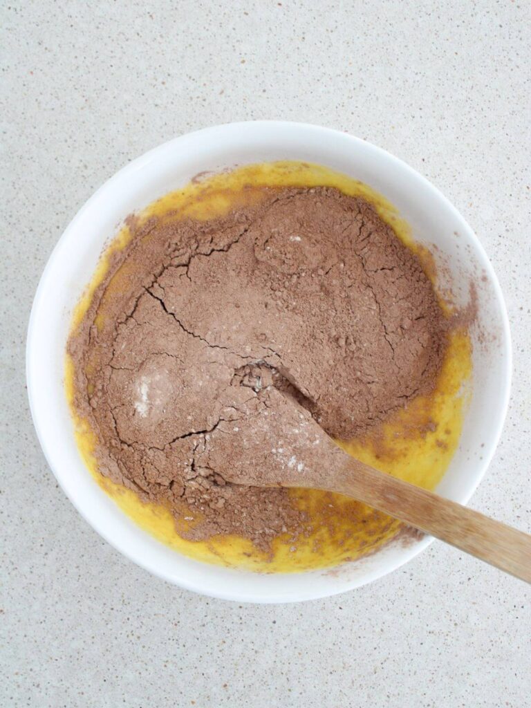 Mixing the wet ingredients with the dry ingredients in a white bowl with a wooden spoon