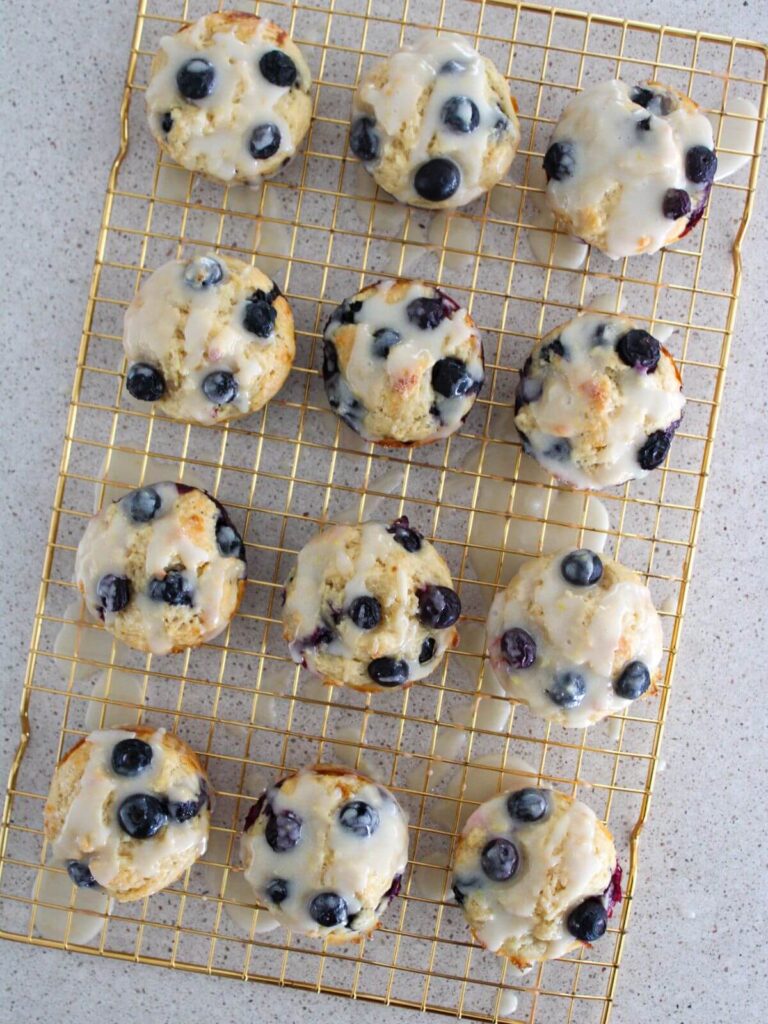 blueberry lemon muffins drizzled with lemon glaze on a golden cooling rack