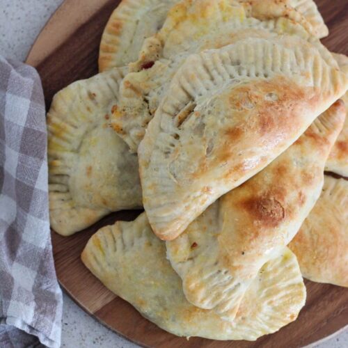 chicken bacon ranch pockets stacked on a wooden cutting board with a plaid napkin next to them