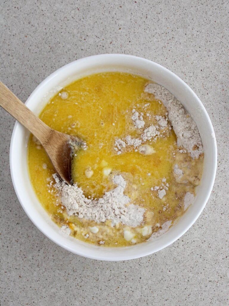 mixing the wet ingredients with the dry ingredients together in a white bowl with a wooden spoon