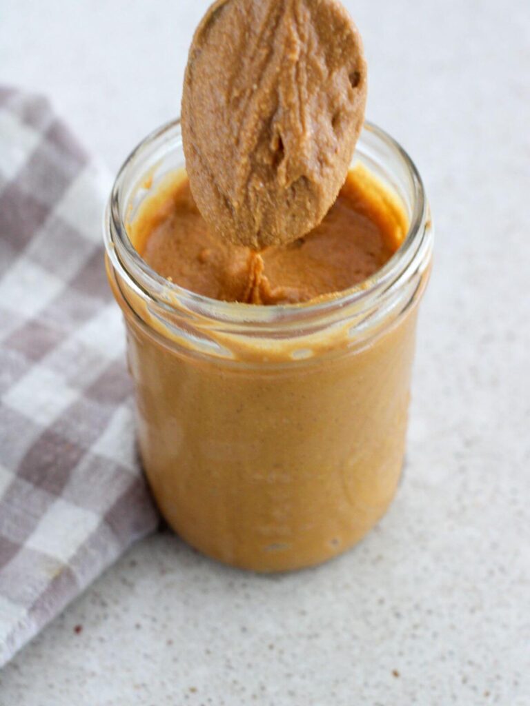 creamy honey peanut butter in a mason jar with peanut butter running off the spoon with a plaid napkin next to it