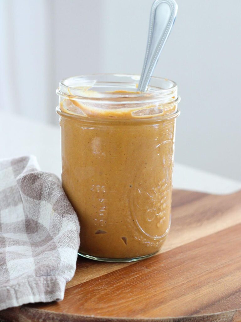 peanut butter in a mason jar with a silver spoon on a cutting board with a plaid napkin