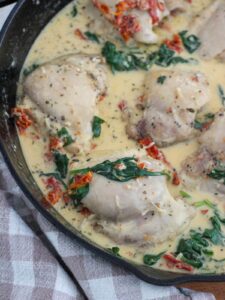 creamy tuscan chicken in a cast iron skillet with a plaid napkin next to it