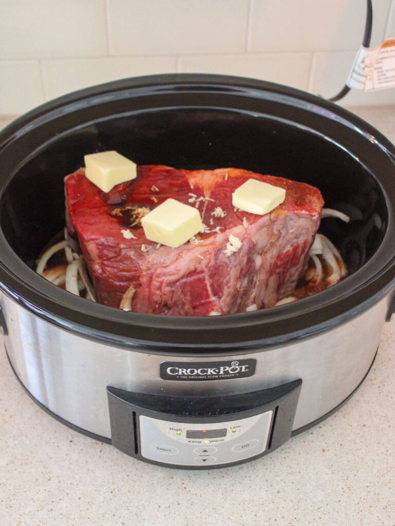Adding butter and liquids to the top of the roast over the onions in the crockpot