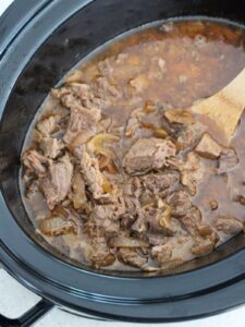 simple crockpot roast beef in a crockpot ready to eat with a wooden spoon